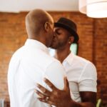 Tedere kus tussen twee mannen met een wit overhemd en een hoed.