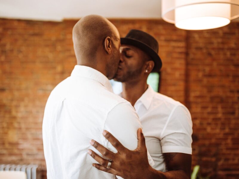 Tedere kus tussen twee mannen met een wit overhemd en een hoed.