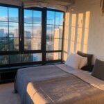 Moderne slaapkamer met groot raam en uitzicht op een stad bij zonsondergang.