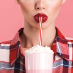 Een vrouw met rode lippenstift drinkt een milkshake door een rietje.