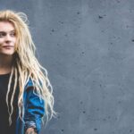 Een blonde vrouw voor een grijze betonnen muur.