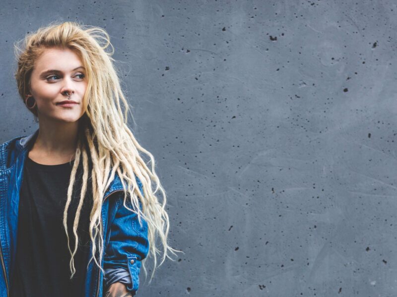 Een blonde vrouw voor een grijze betonnen muur.